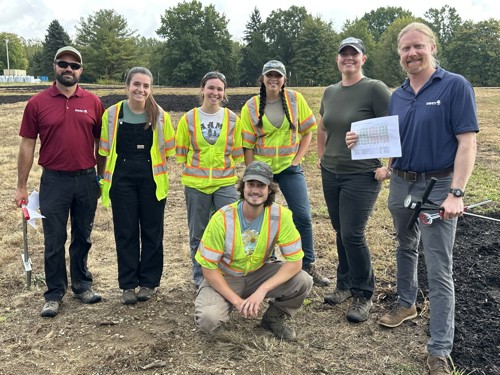 A team of seven Davey employees smiling for a group photo within the compact soil plot.